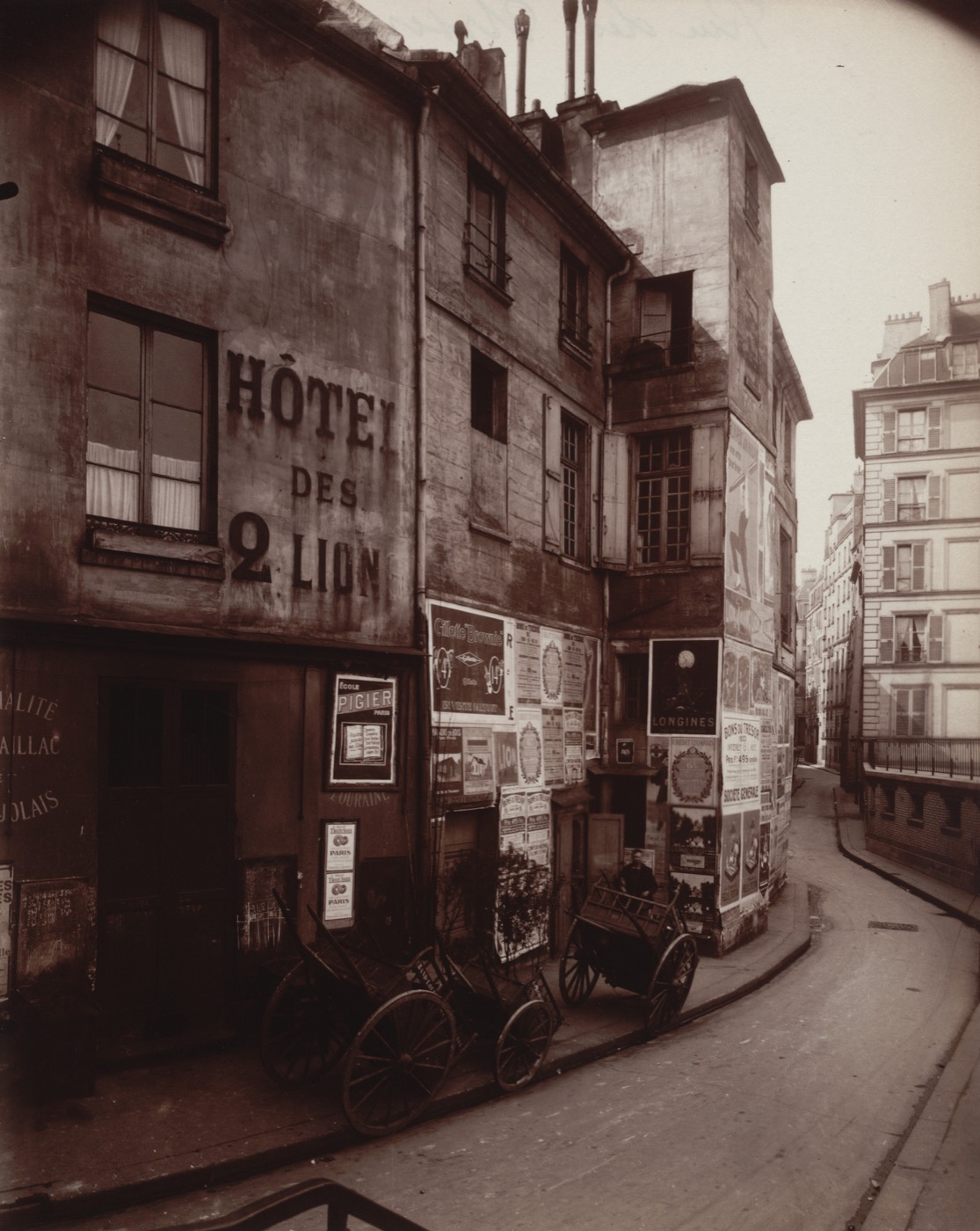 An old curving street with weathered buildings, a painted hotel sign, layered posters and parked handcarts