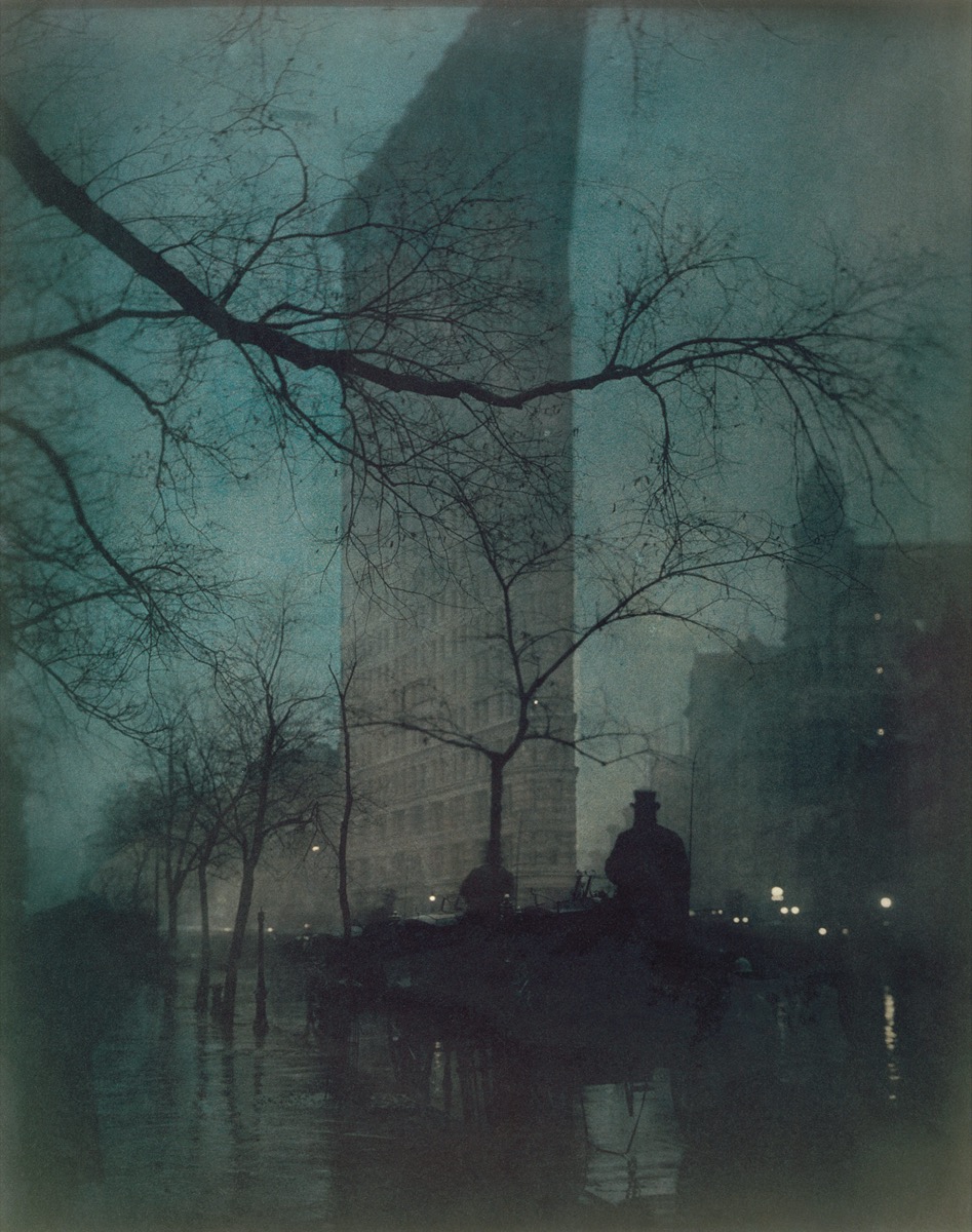 A tall building fading into blue-green dusk behind bare tree branches, a carriage driver silhouetted on a wet street