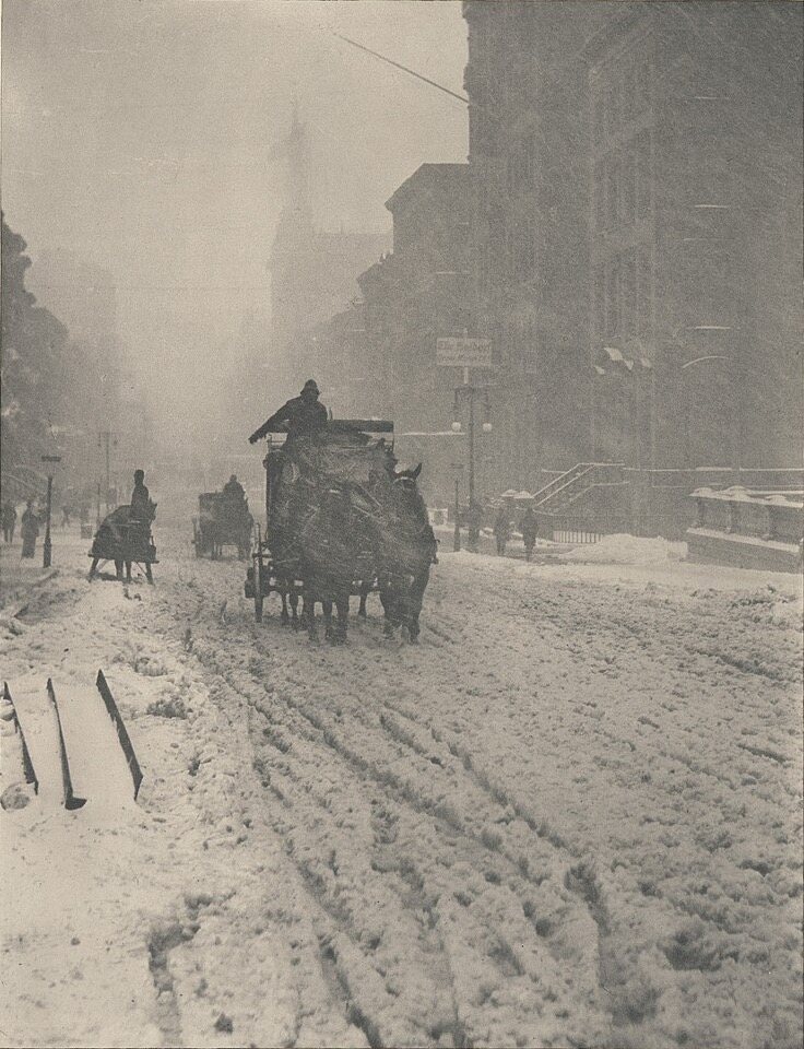 A horse-drawn carriage pushing through deep snow on a city avenue, buildings fading into the storm