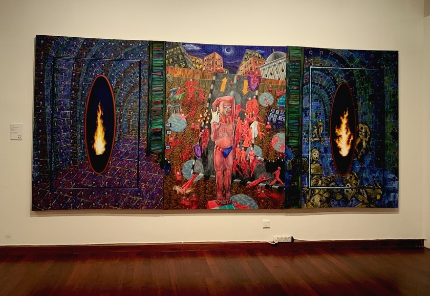 A large three-panel painting on a gallery wall: two side panels with flames inside dark oval portals, a centre panel crowded with red figures in a city at night