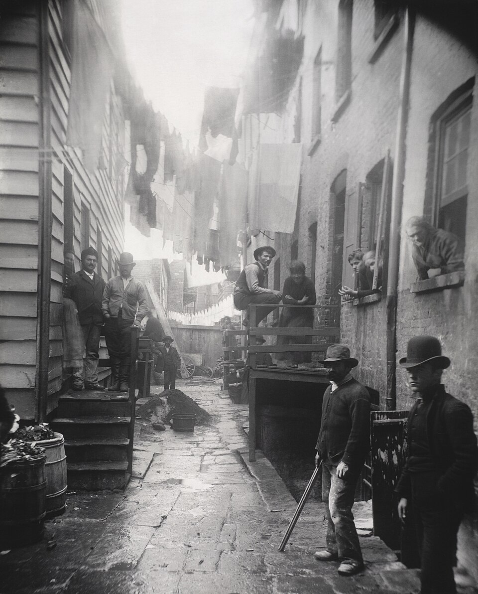 A narrow crowded alley lined with old buildings, people standing and staring at the camera