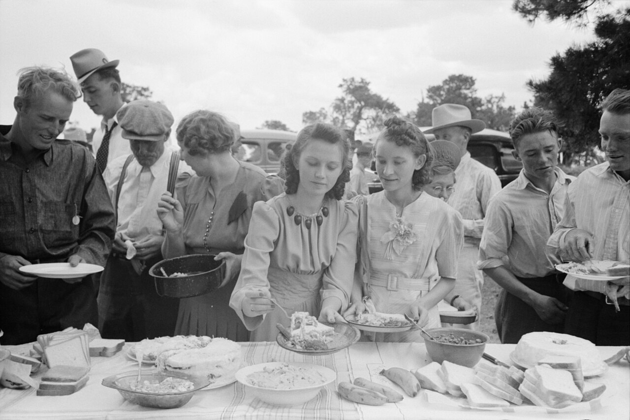 Neighbours serving each other food at a long outdoor table