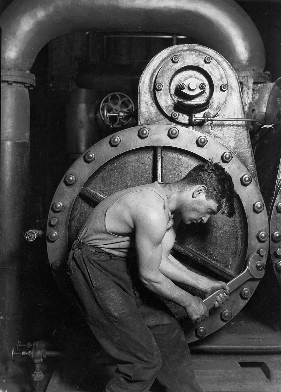 A mechanic bending over a giant steam pump, tightening a bolt with a wrench